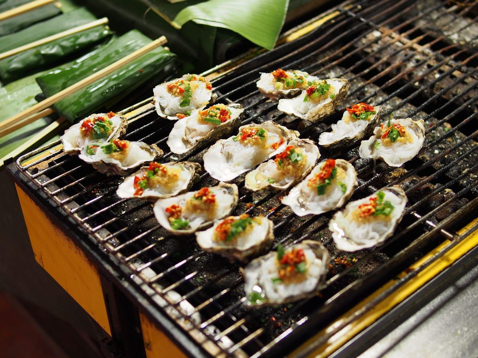 Grilled oysters topped with scallion oil and crushed peanuts on a charcoal grill