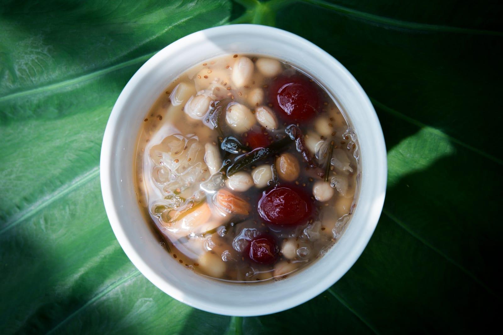 A bowl of chè thập cẩm with white beans, red jelly pearls, longan and lotus seeds in light syrup.